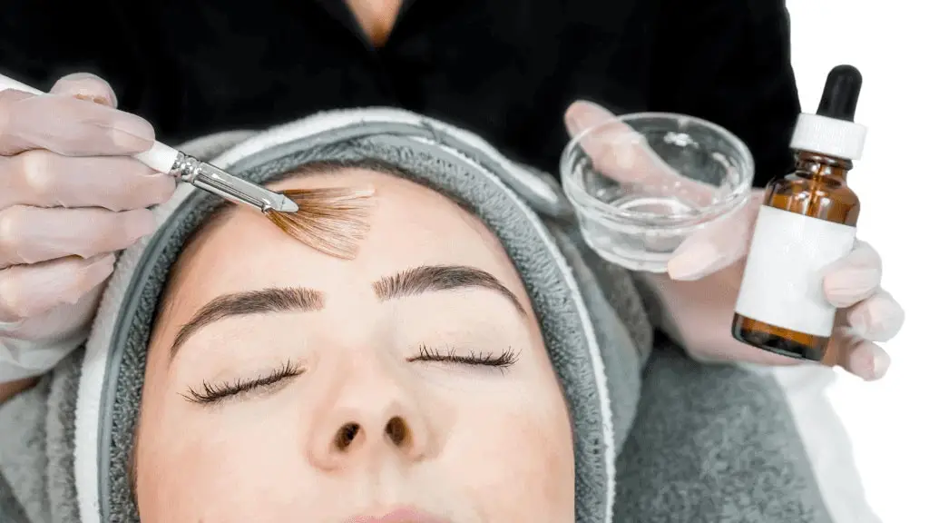 Close up of beautician (cosmetologist) applying chemical peel treatment on patient in a beauty spa, for skin rejuvenation, complexion and acne beauty treatments.