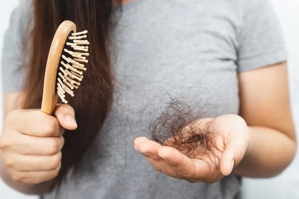 woman with a clump of hair in one hand and a hairbrush in her other ohand