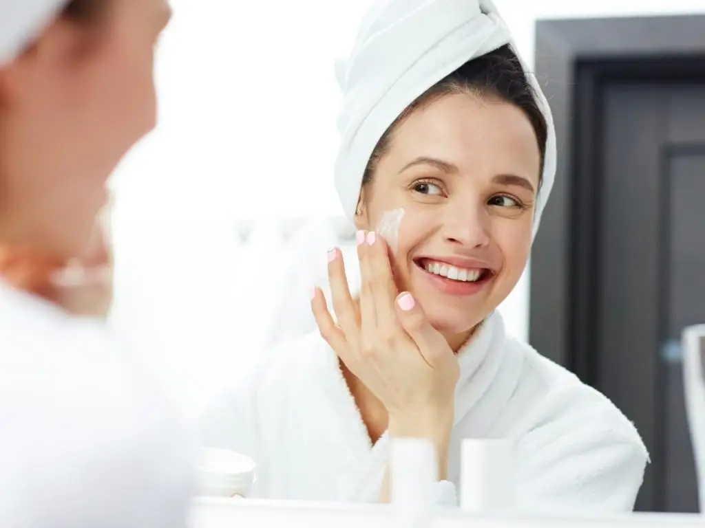 woman applying skin cream to face in mirror